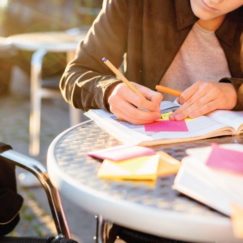 Photo - up close of young woman's hand writing notes at a small table