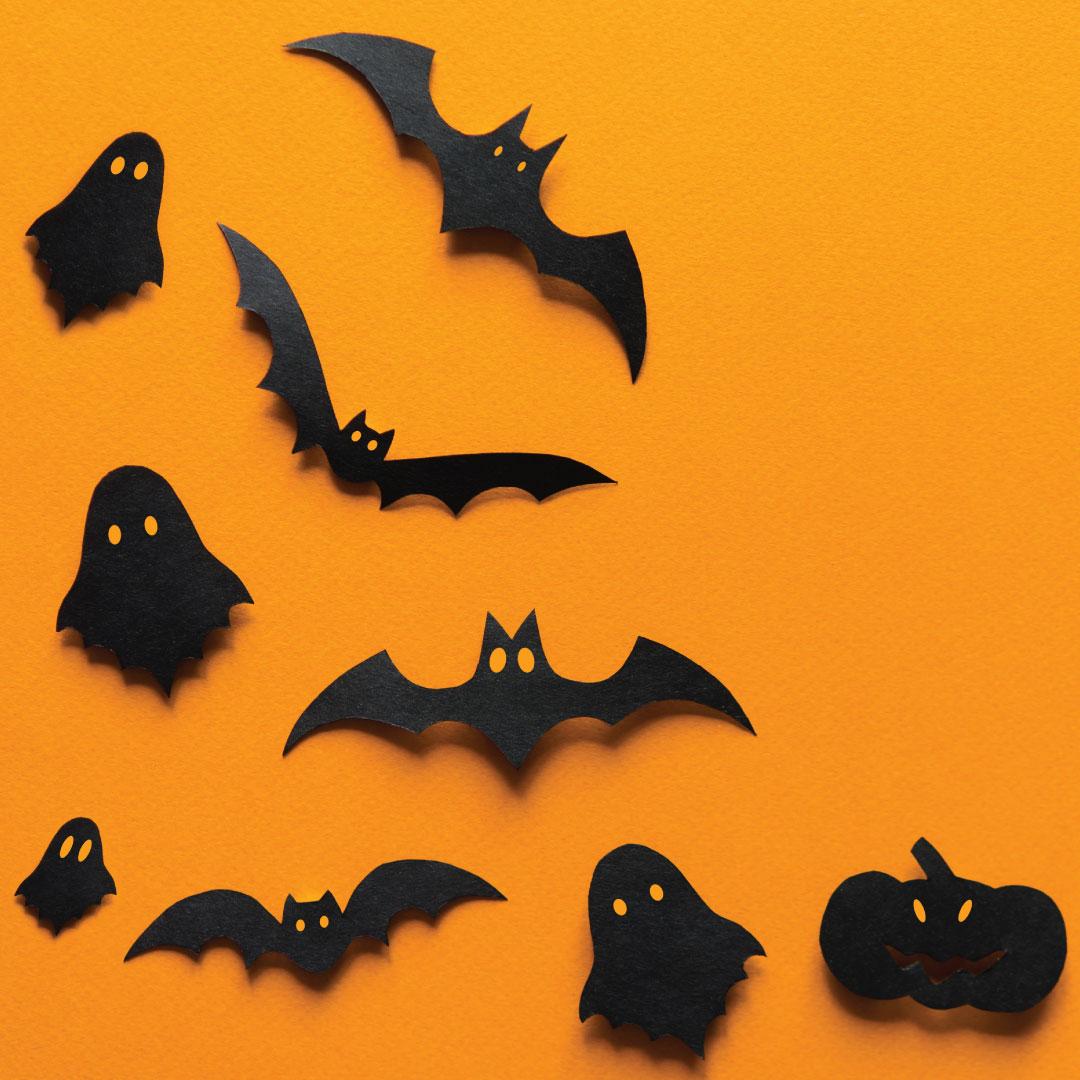 Black paper cutouts of bats, pumpkins & ghosts on orange background